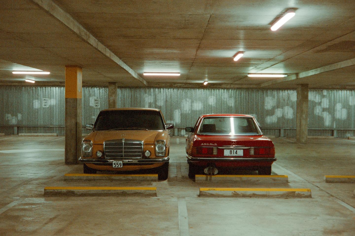 Two vintage cars are parked facing opposite directions in an underground parking garage.