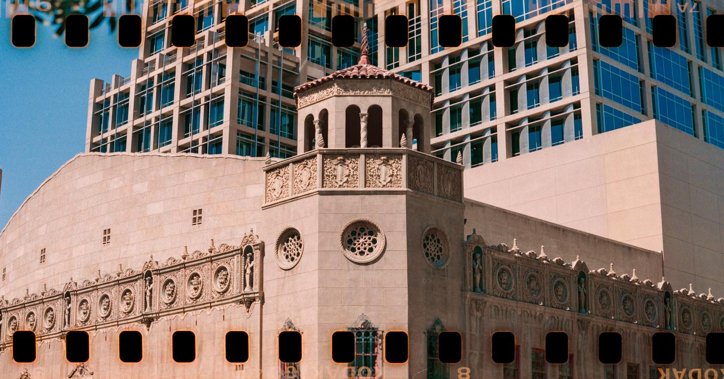 An ornate building with a tower and a modern building with blue windows are visible against a clear sky.