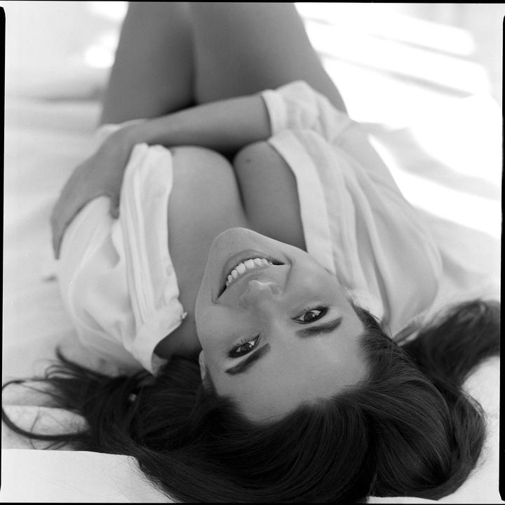 A woman with long hair smiles at the camera while lying on her back.