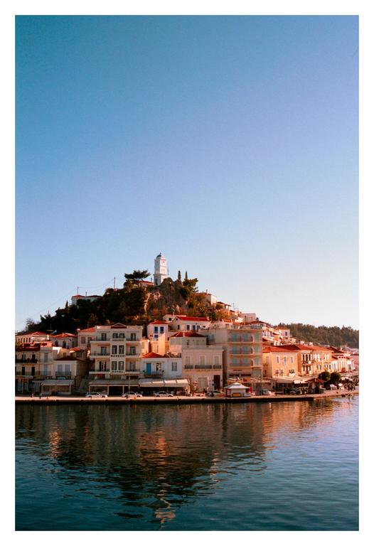 A town with white buildings and red roofs is built on a hill next to a body of water, with a white clock tower visible at the top of the hill.