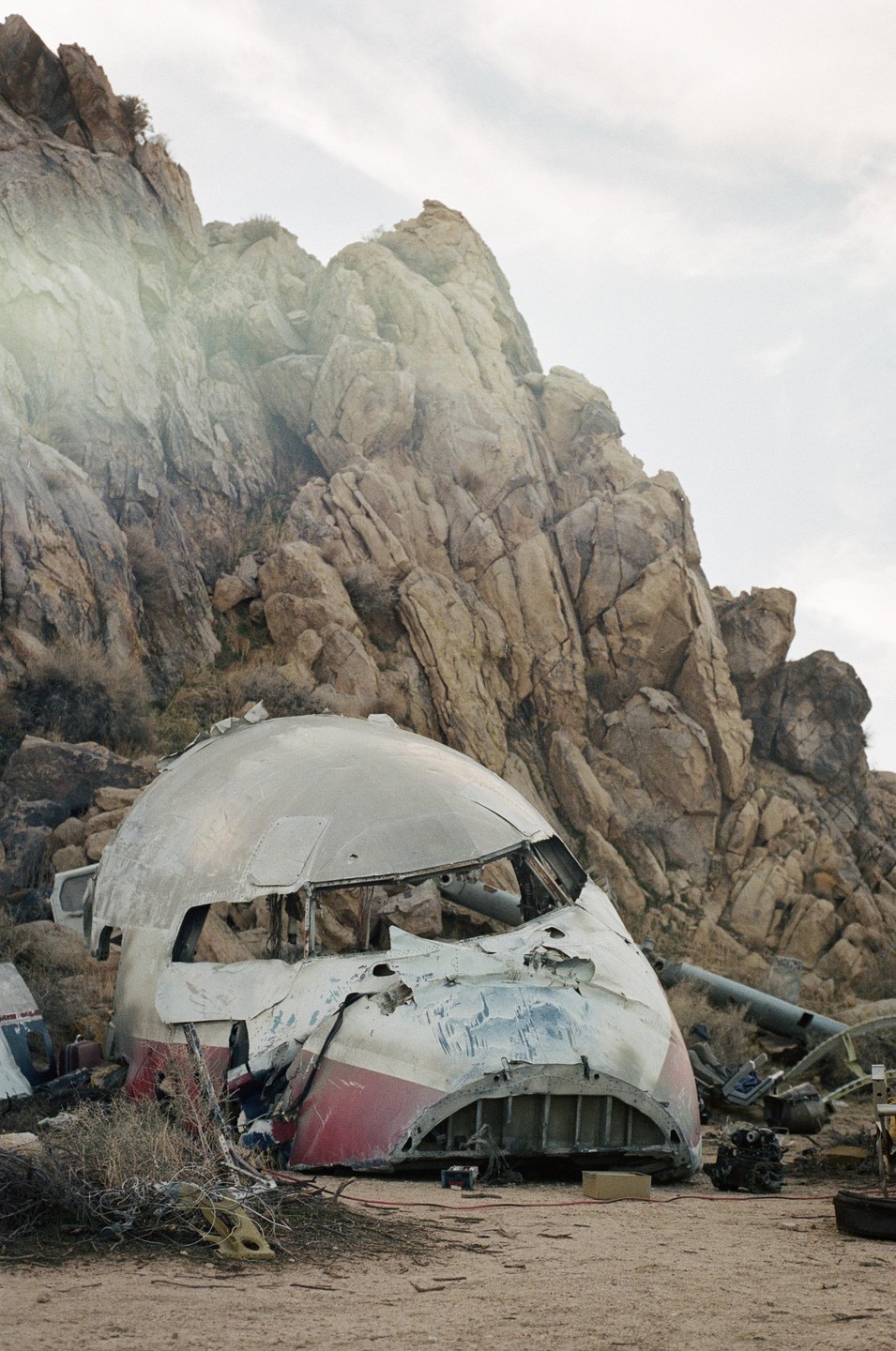 The wreckage of an airplane fuselage lies on the ground in front of a rocky mountain.