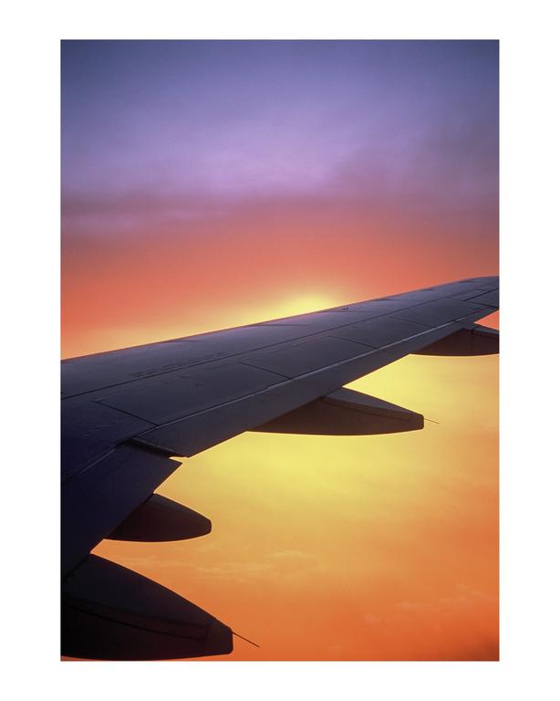 An airplane wing is silhouetted against a vibrant sunset sky.