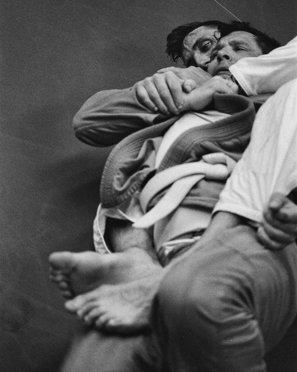 Two men are grappling in a close-up, black and white shot.
