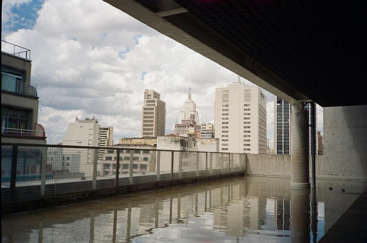 A cityscape with tall buildings is reflected in a large puddle on a rooftop.