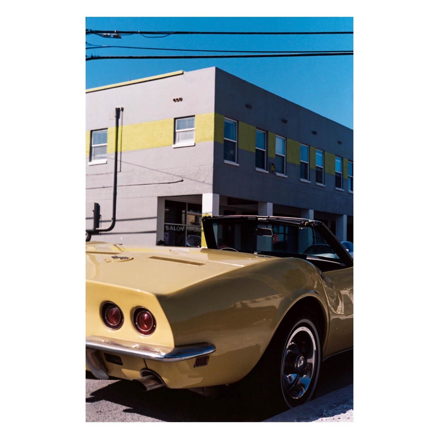 A yellow convertible car is parked on a street in front of a building with a yellow stripe.