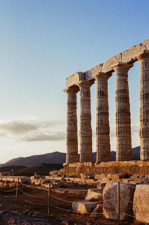 Ancient stone columns stand against a clear sky with mountains in the distance.