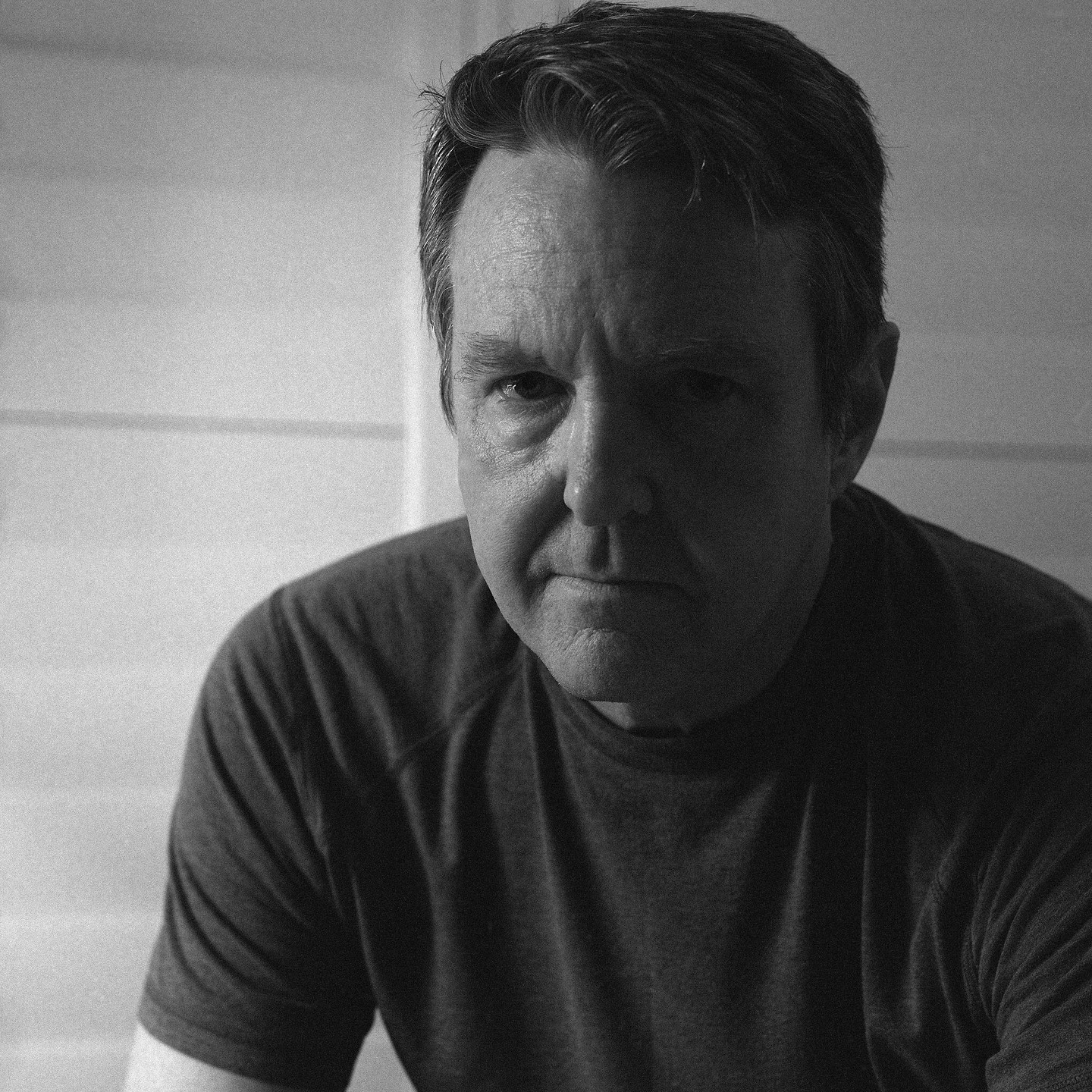 A man with short hair looks directly at the viewer in a self-portrait.