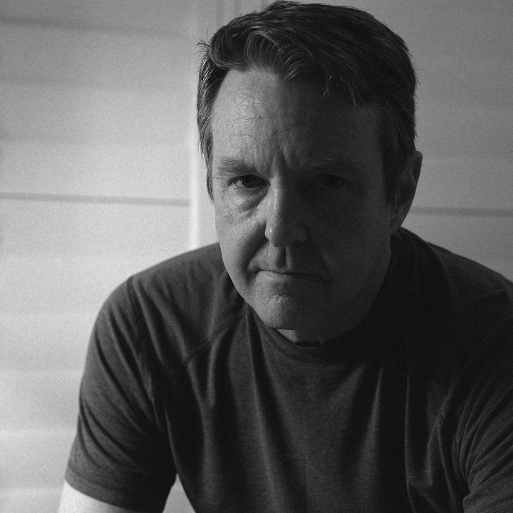 A man with short hair looks directly at the viewer in a self-portrait.