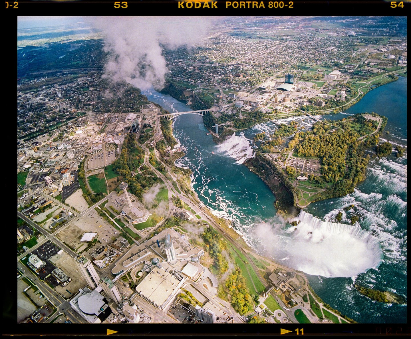 An aerial view shows the Niagara Falls with surrounding urban areas and a bridge over the river.