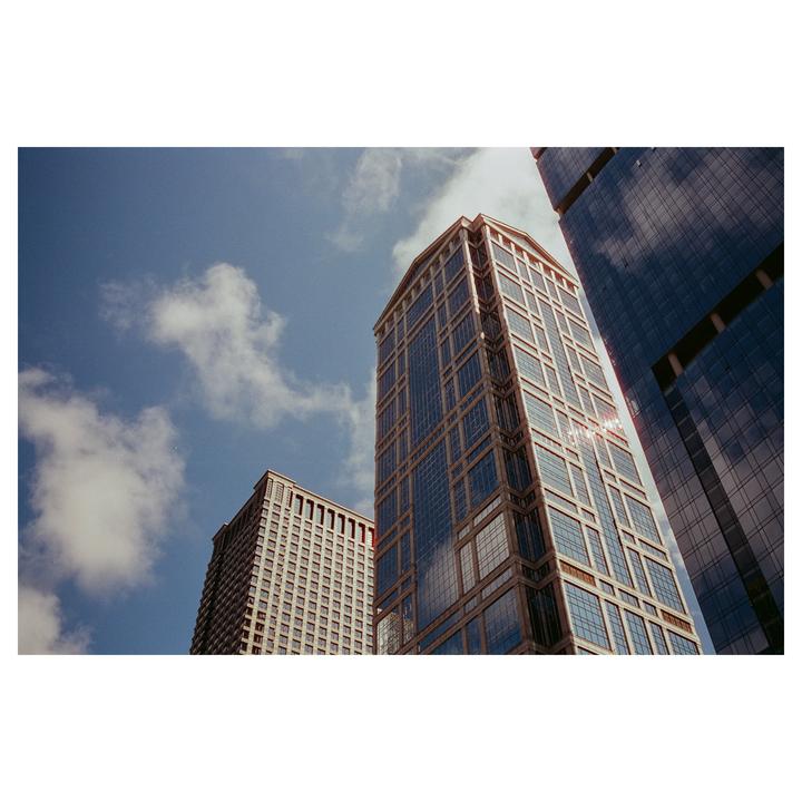 Three tall buildings with many windows are visible from a low angle against a blue sky with clouds.