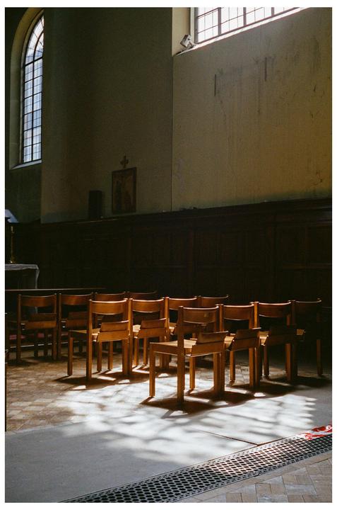 Sunlight streams through a tall arched window, illuminating a row of wooden chairs in a church.