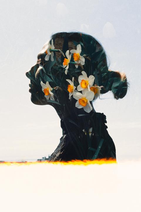 A woman's profile is double exposed with white and orange flowers and green foliage.