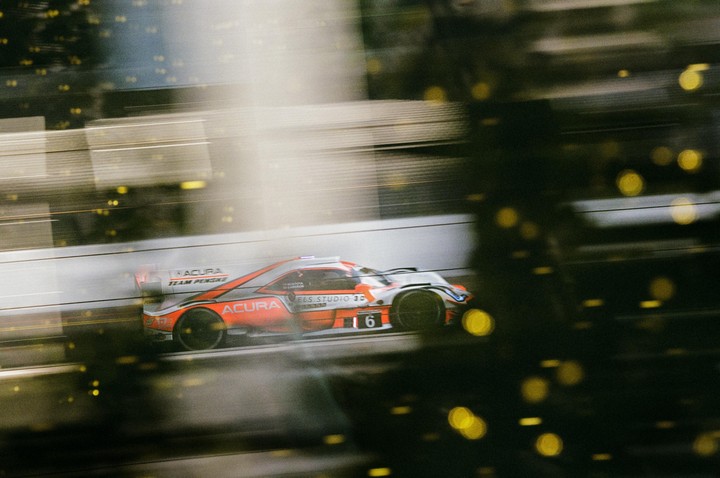 A race car with the number 6 is captured in motion blur with bokeh lights in the foreground.