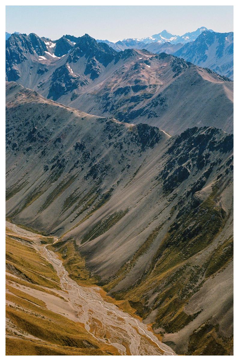 A winding riverbed flows through a valley surrounded by steep, rocky mountains.