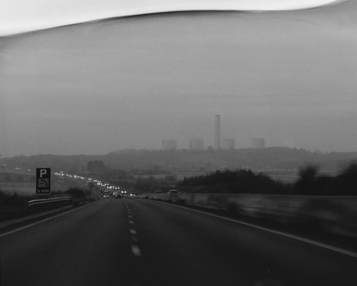 A highway stretches into the distance with cars and a power station under a hazy sky.