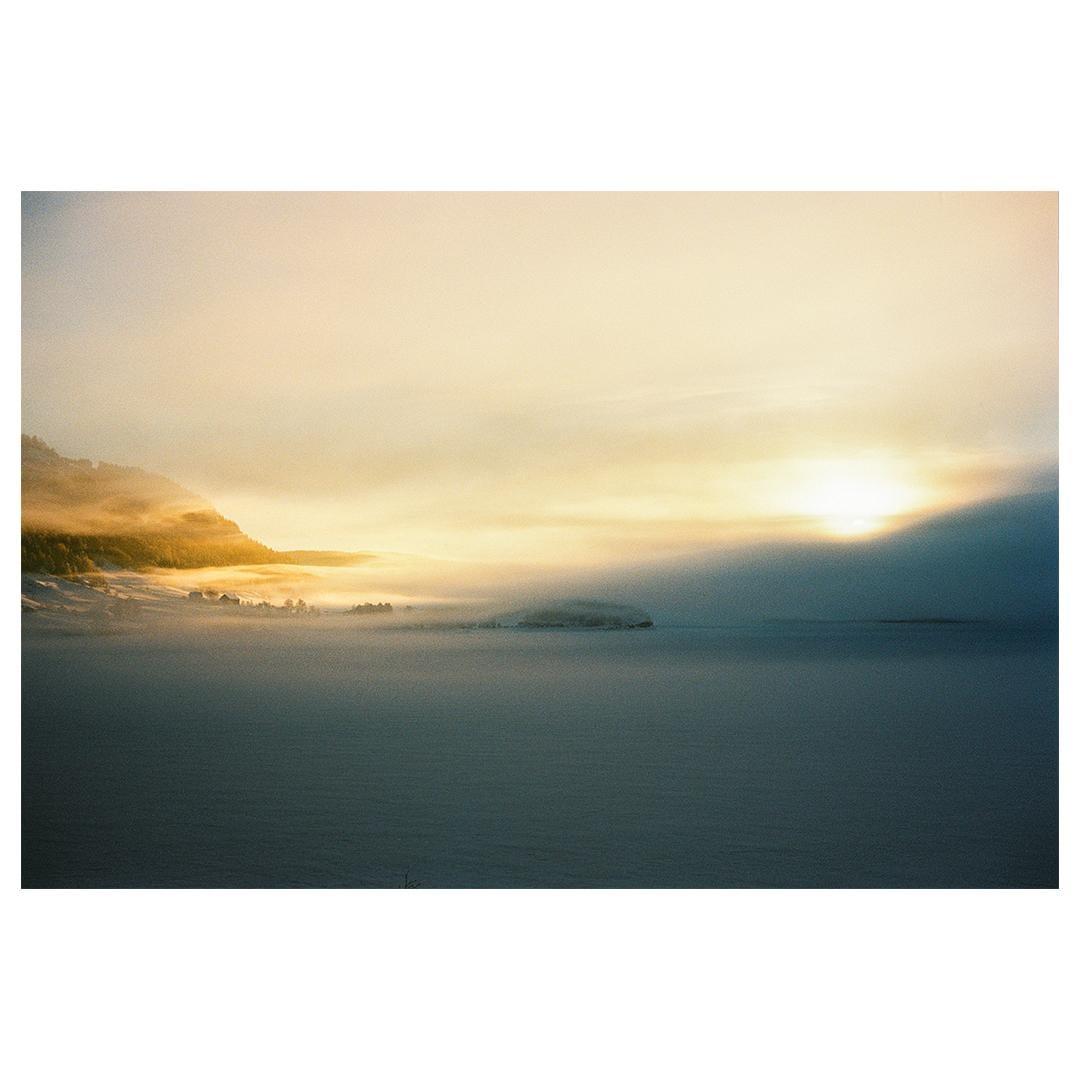 A hazy winter landscape shows a sunlit mountain and a frozen lake.