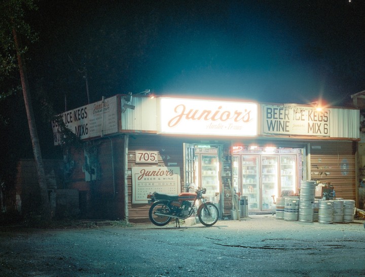 A motorcycle is parked in front of a store with a bright "Junior's" sign at night.