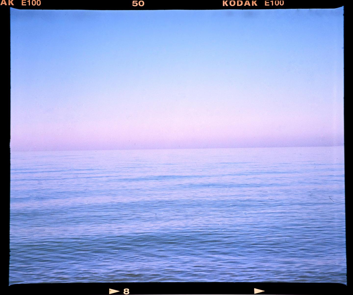 The calm water of Lake Michigan meets a pastel sky at the horizon.