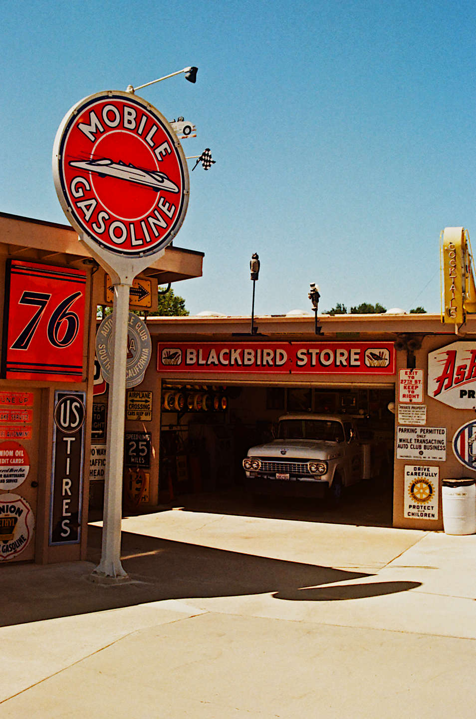 A vintage Mobile Gasoline sign stands prominently in front of a store with a white pickup truck parked inside.
