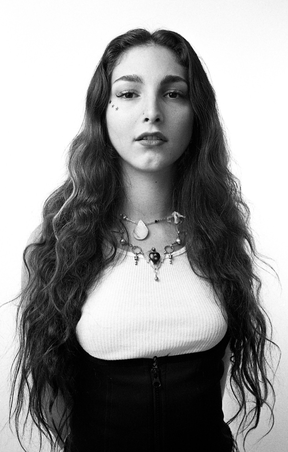 A woman with long, wavy hair and a necklace looks directly at the viewer.