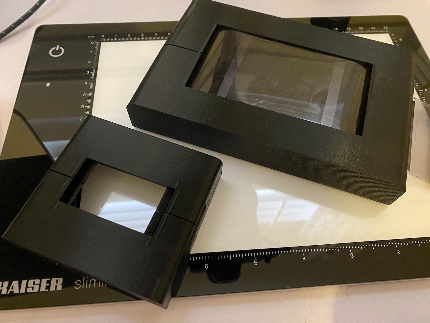 Two black 3D-printed film scanner holders are on top of a light pad with a ruler.