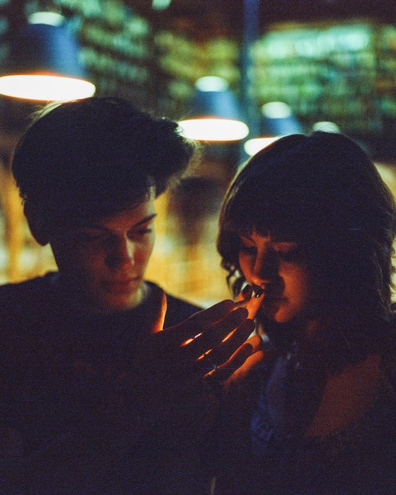 A couple is illuminated by a warm light source, with one person holding their hand over the light.