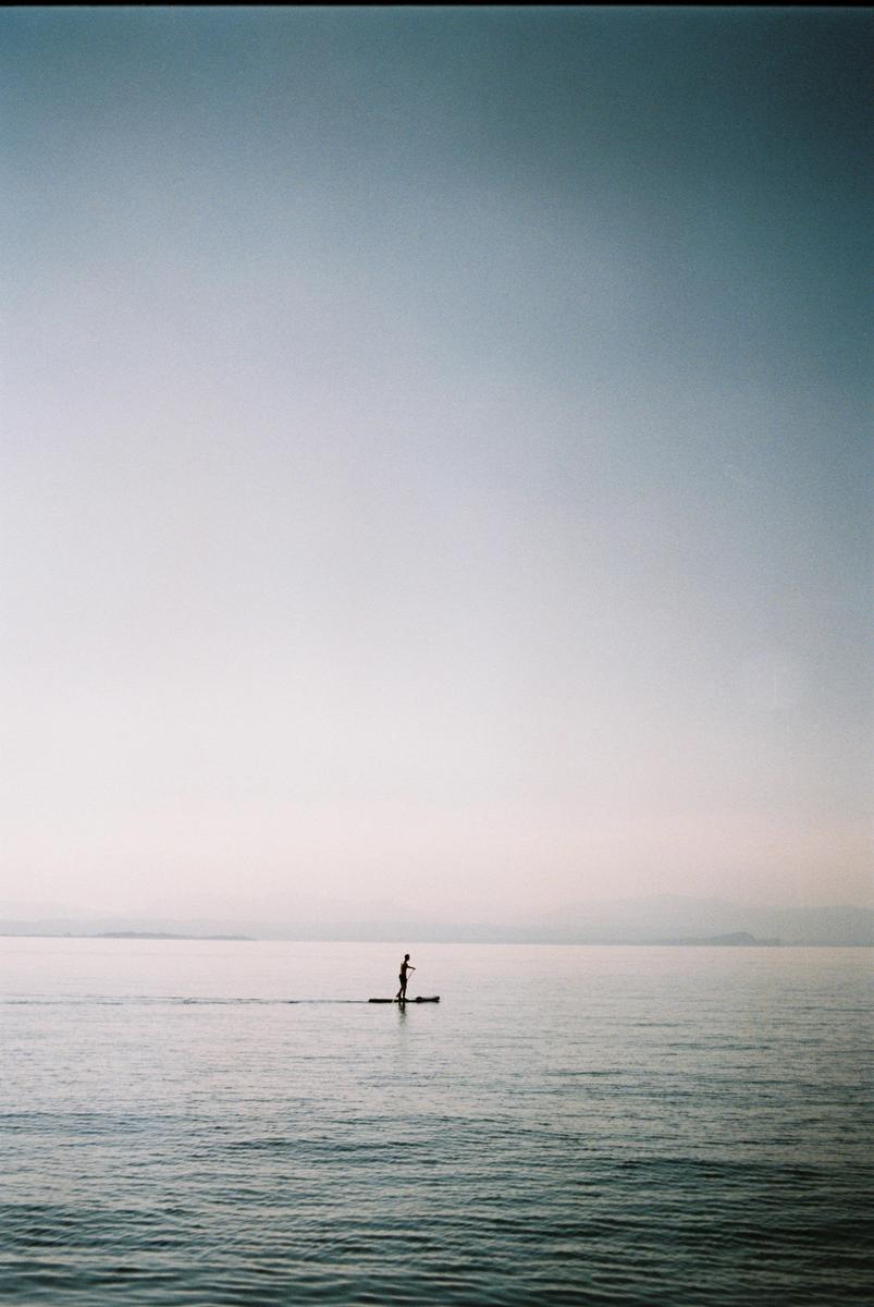 A person stands on a paddleboard in the middle of a calm body of water under a hazy sky.