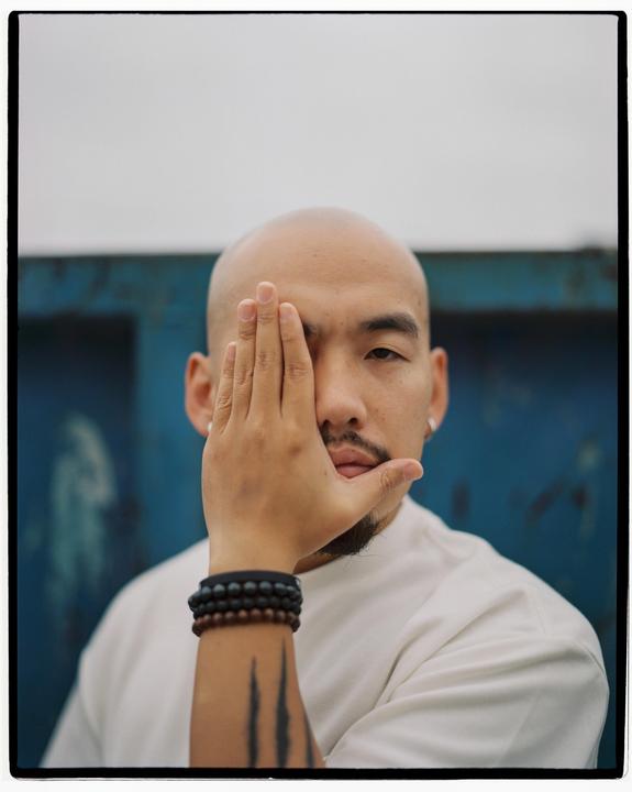 A man with a shaved head covers half his face with his hand.