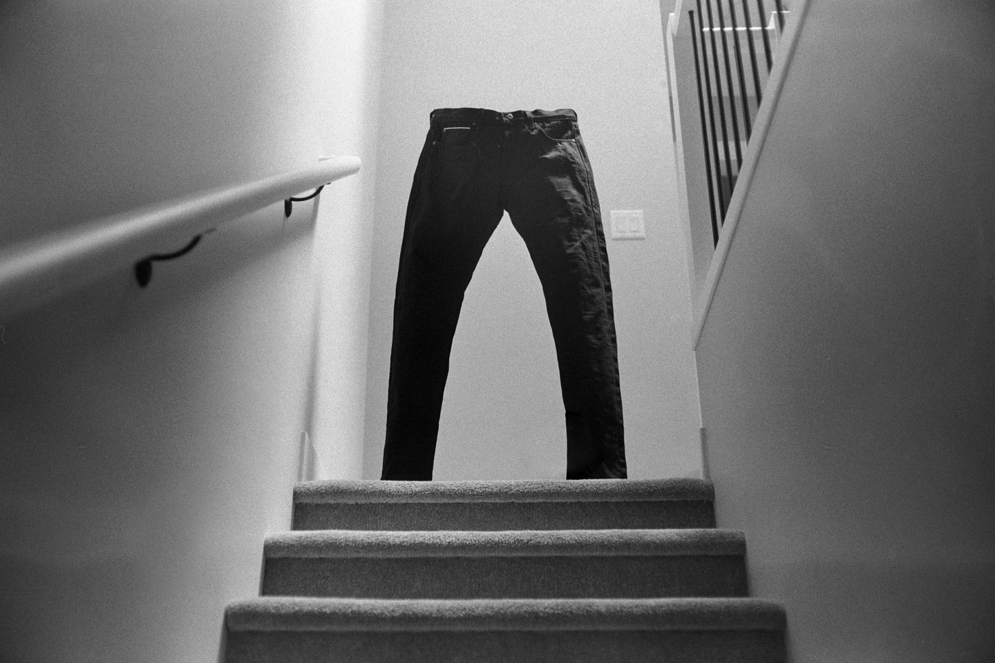 A pair of pants stands upright on a carpeted staircase in a black and white image.