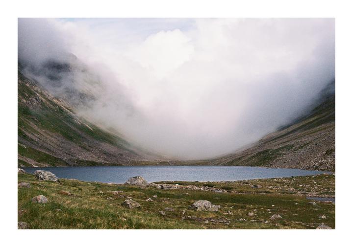A lake is nestled between two mountains with clouds descending into the valley.