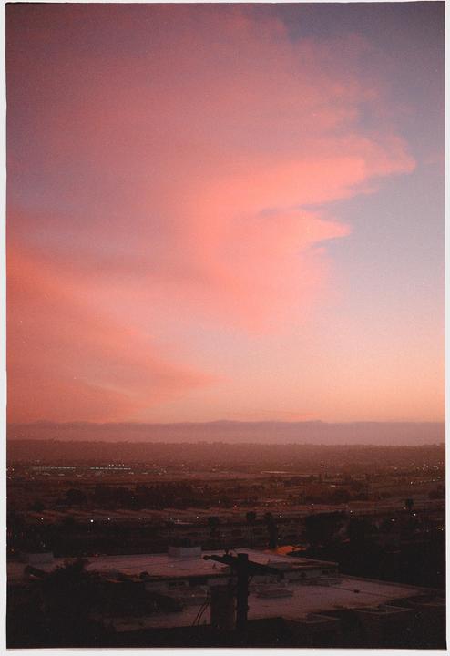 A vibrant pink and orange sunset sky hangs over a city with distant mountains.