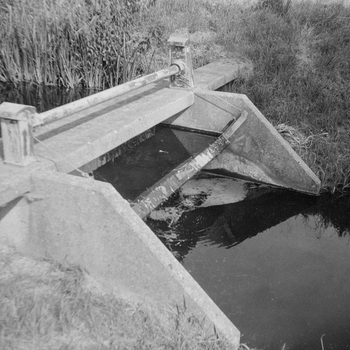 A concrete lock with a metal bar across it is surrounded by water and grass.