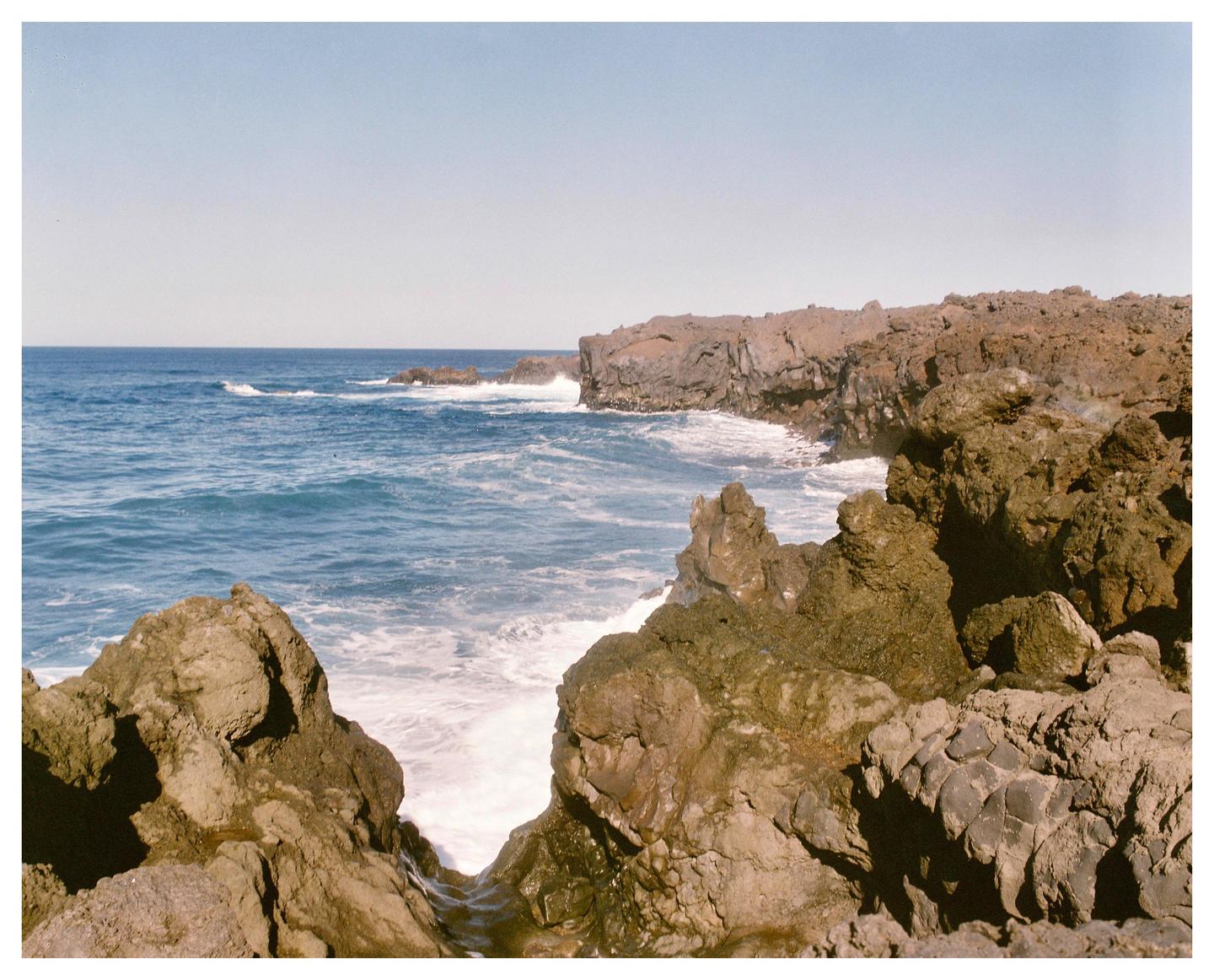 Waves crash against a rocky coastline under a clear sky.