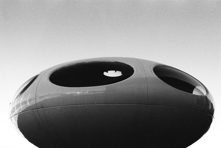 A black and white image shows a close-up of a futuristic, oval-shaped structure with multiple circular windows.
