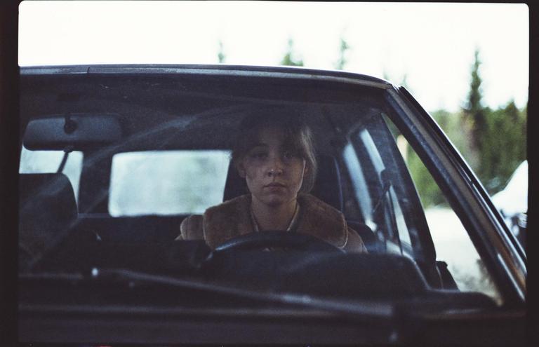 A young woman with a dirty face is sitting in the driver's seat of a car.
