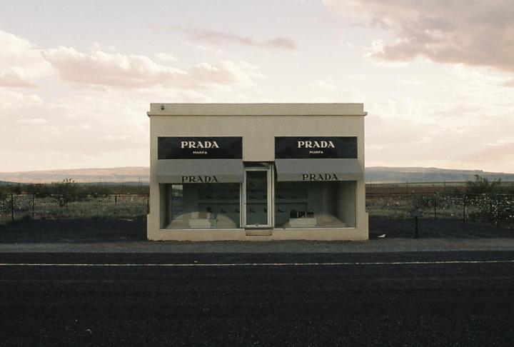 A Prada storefront stands alone on a flat landscape under a cloudy sky.