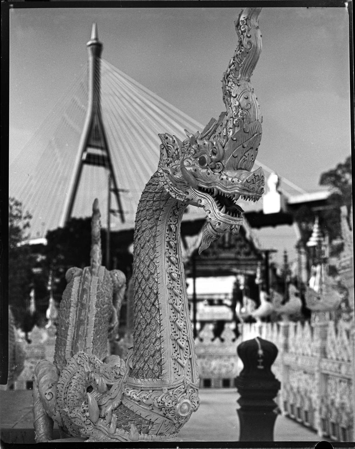 A statue of a mythical creature with a dragon-like head and a scaly body stands in front of a cable-stayed bridge.