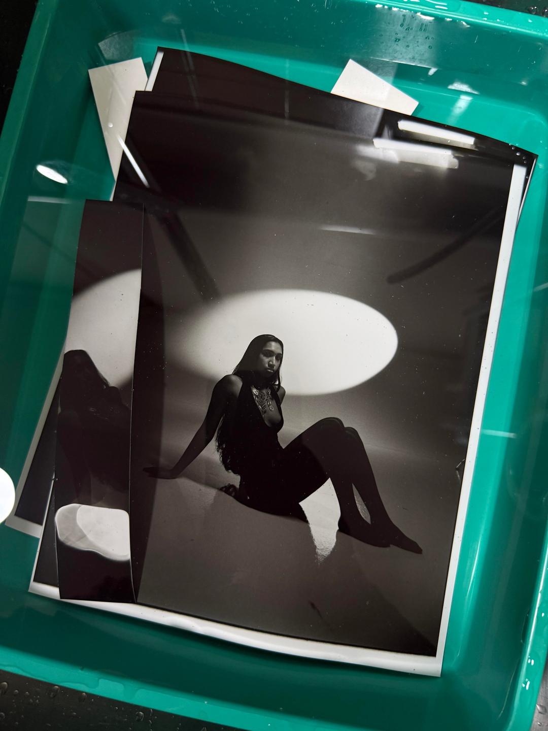 A black and white print of a woman in a dark dress is seen in a developing tray.
