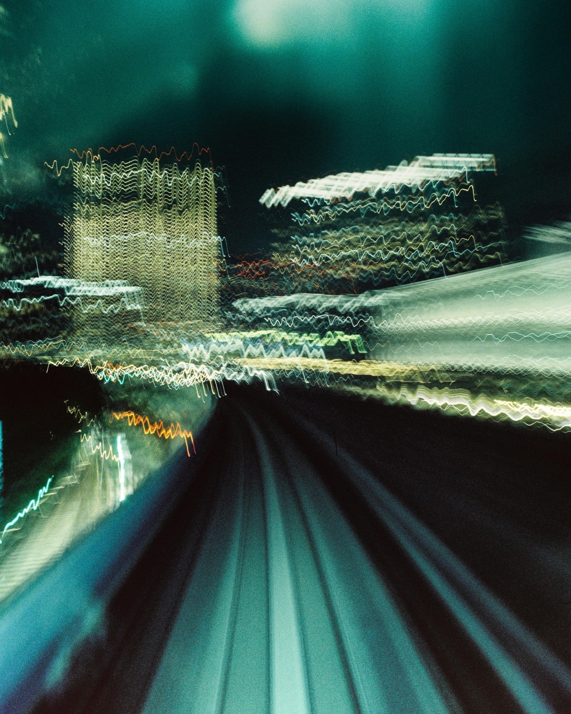 Light trails from buildings and a road are blurred by motion at night.