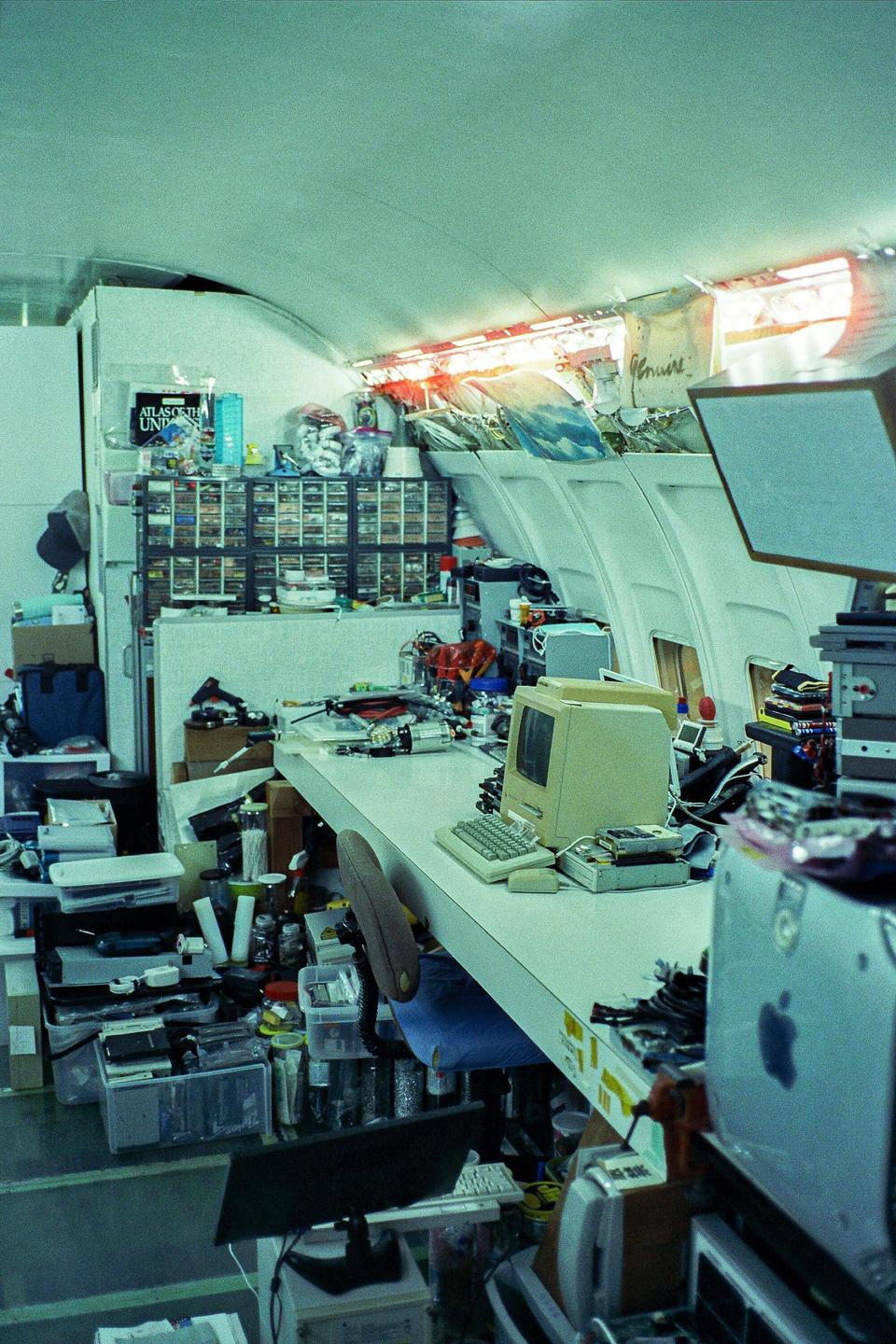 A cluttered room with computer equipment and storage containers is illuminated by bright light from a window.