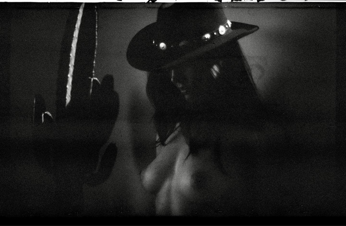 A woman wearing a hat is visible in a dark, grainy, black and white portrait.