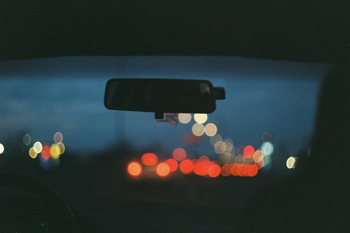 A car's rear view mirror is visible against a dark blue sky with blurred lights in the distance.