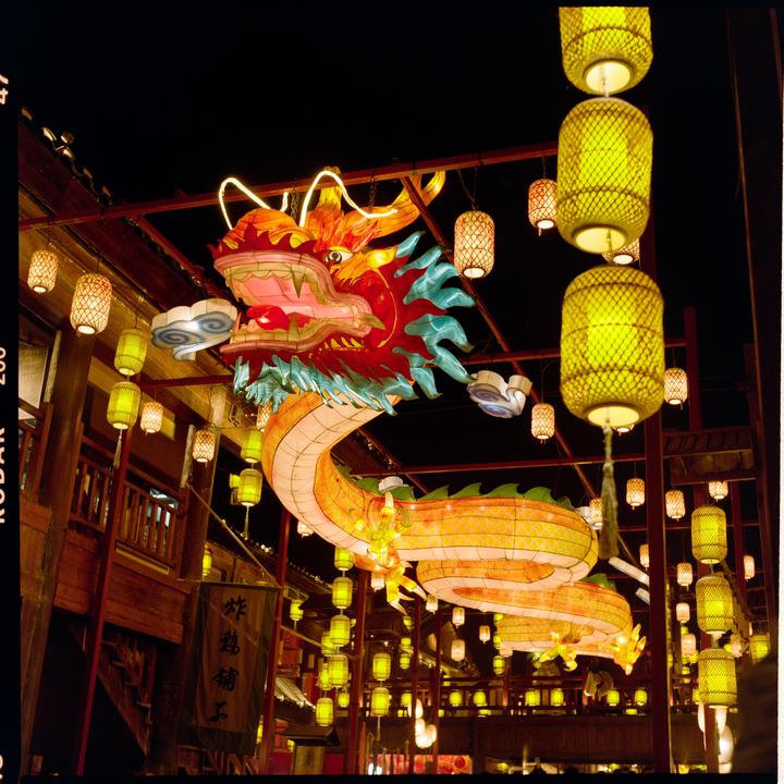 A large, colorful dragon lantern is suspended above a street lined with numerous glowing lanterns and traditional buildings at night.