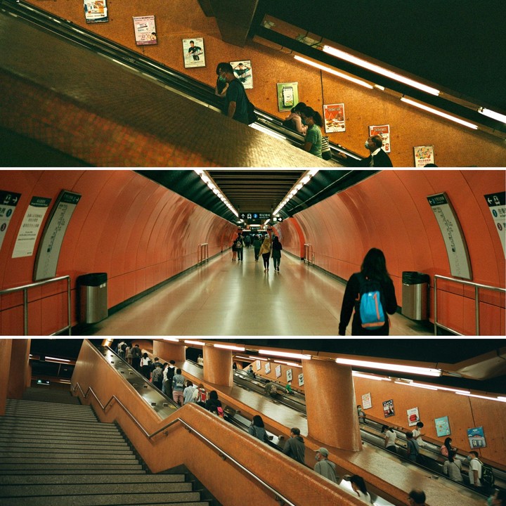 People walk through a subway station tunnel and ride escalators.