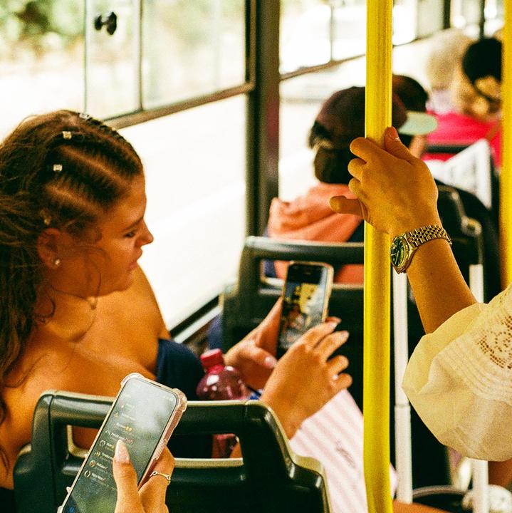 A woman with braided hair looks to the side while holding a phone on a bus.