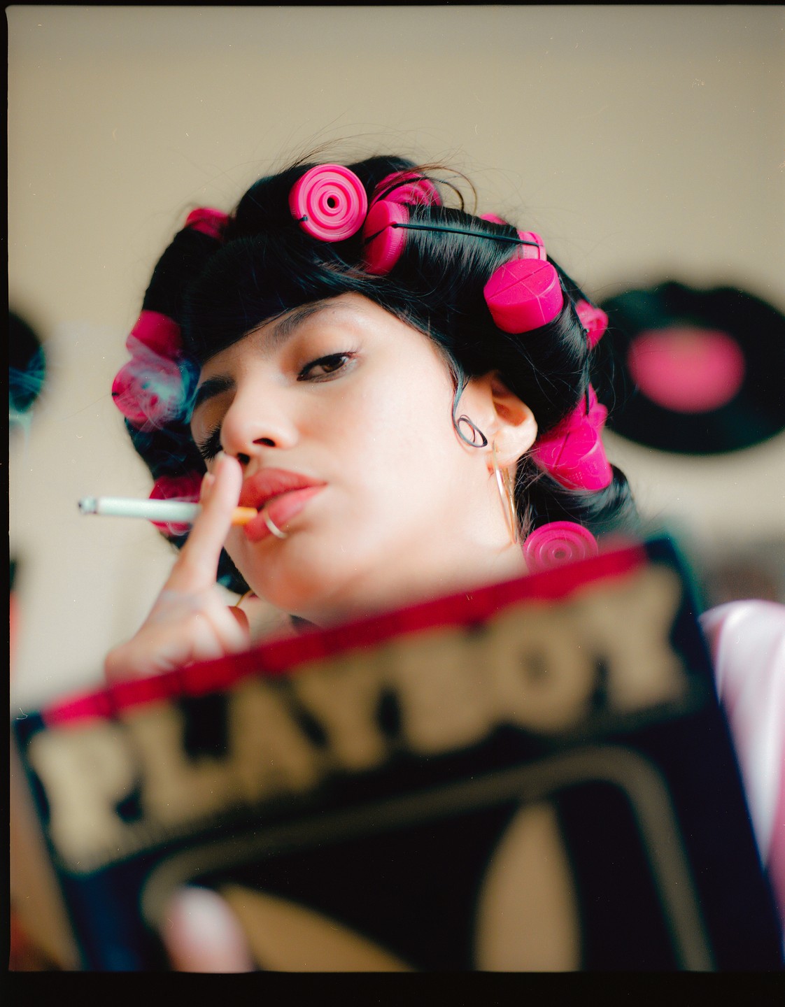 A woman with pink hair rollers smokes a cigarette and holds a Playboy magazine.
