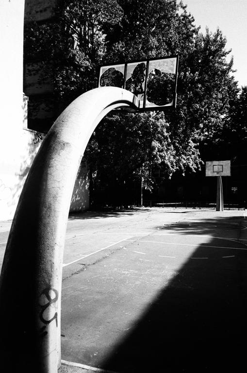 A basketball court is visible with a large, curved concrete support in the foreground and another basketball hoop in the background.