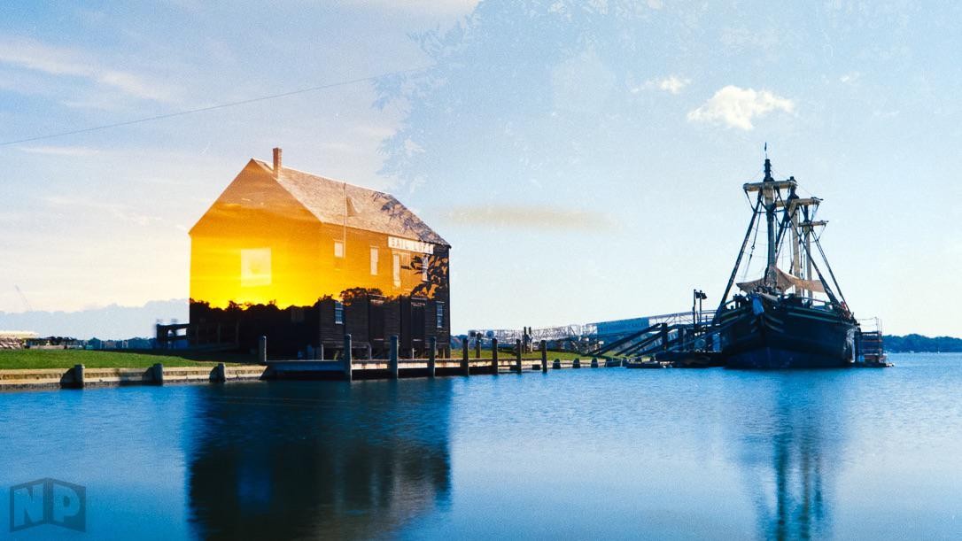 A double exposure shows a sunset over a building and a ship docked in the water.