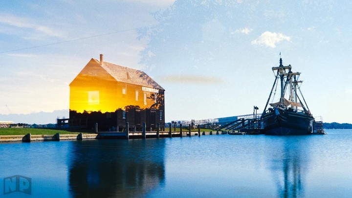 A double exposure shows a sunset over a building and a ship docked in the water.
