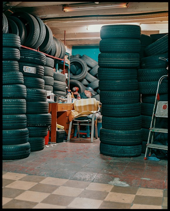 A man sits at a desk surrounded by stacks of tires in a garage.